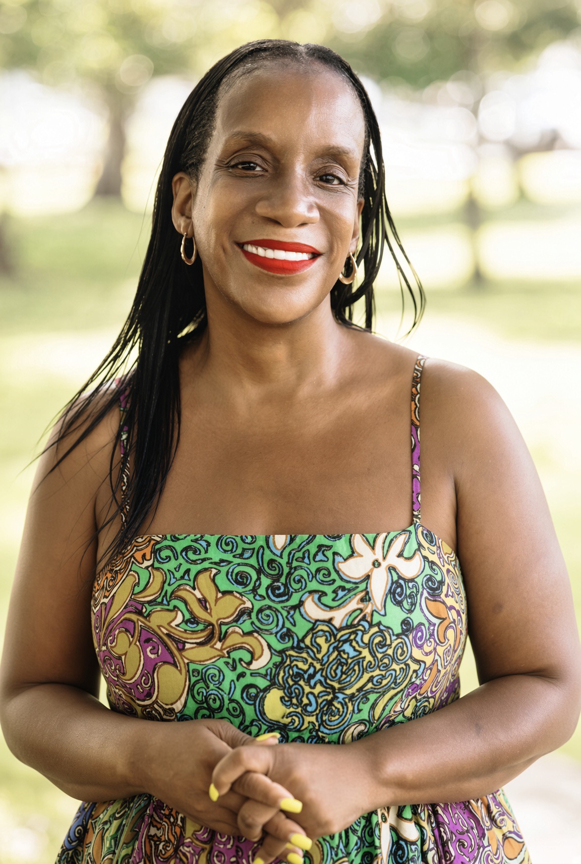 Charisa D. Strong smiling warmly, standing outdoors in a green and purple print dress